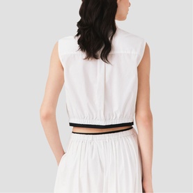 Model wearing Maje metallic white sleeveless crop top with elasticated hem and navy trim detail, styled with matching white skirt, back view.
