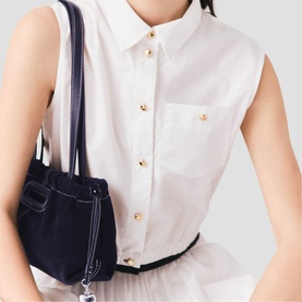 Model carrying Maje bag in navy blue with gold-tone hardware, styled with a white sleeveless button-up shirt and black belt.