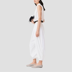 Model wearing white sleeveless crop top and draped wide-leg trousers, carrying black clutch, styled with checked slip-on flats