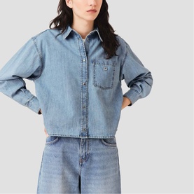 Model wearing Maje cropped light blue denim shirt with chest pocket, paired with light wash wide-leg jeans