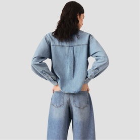 Model wearing Maje light blue denim jacket with long sleeves and back pleat detail, styled with wide-leg denim jeans, rear view