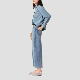 Model wearing Maje denim jacket and wide-leg jeans in light blue, styled with white patterned ballet flats and a small woven bag