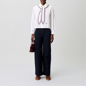 Model wearing Claude Pierlot white shirt with contrast trim bow detail and navy wide-leg trousers, styled with burgundy bag and tan shoes.