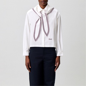 Model wearing Claude Pierlot white cropped shirt with contrast stripe-trimmed bow tie detail and script logo, styled with navy trousers.