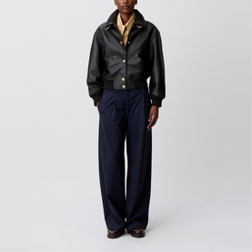 Model wearing Claude Pierlot black lambskin Leather Bomber Jacket with gold-tone press studs, styled with navy wide-leg trousers and a yellow shirt.