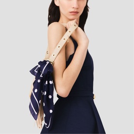 Model carrying Maje navy dots print bag with cream strap and gold-tone hardware, styled with a navy strapless dress