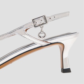 Maje silver metallic slingback heels with buckle ankle strap, charm detail, and slender stiletto heel, tan leather insole visible