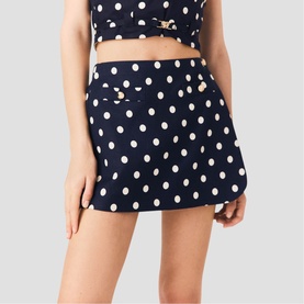 Model wearing Maje navy dots print mini skirt with gold buckle detail, styled with matching polka dot crop top