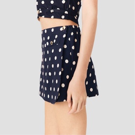 Model wearing Maje navy dots print shorts with matching cropped top, high-waisted silhouette with gold button detail