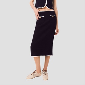 Model wearing Maje black knit midi skirt with cream frill trim and front pockets, styled with matching crop top and beige loafers