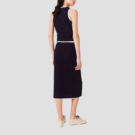 Model wearing Maje Womens French Dress in navy with white trim detailing, sleeveless midi length, back view, styled with beige flats