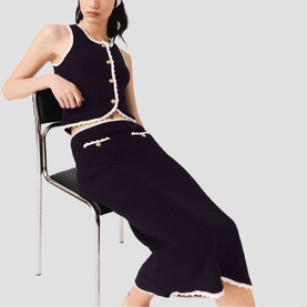 Model wearing Maje Womens French Dress in navy with contrast white trim, pearl button detail and scalloped hem, seated on chrome chair