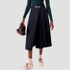 Model wearing Maje navy midi wrap skirt with belt detail, styled with green long-sleeve top and beige shoes, carrying dark red bag