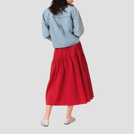 Model wearing Maje Womens French Dress in red, gathered midi skirt silhouette, styled with light blue denim jacket and white mules, back view.