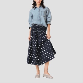 Model wearing Maje navy dots print midi skirt with elasticated waist, styled with a light blue denim shirt and silver flat shoes.