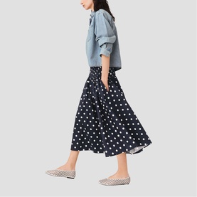 Model wearing Maje navy dots print midi skirt with full pleated silhouette, styled with light blue shirt and check flats.