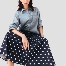 Model wearing Maje Womens French Dress in navy dots print, styled with a light blue denim shirt, seated pose.