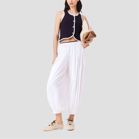 Model wearing Maje white wide-leg pleated trousers with navy cropped vest, styled with beige lace-up shoes and tan bag
