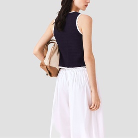 Model carrying a tan backpack with gold hardware, styled with a navy sleeveless top and white wide-leg trousers.