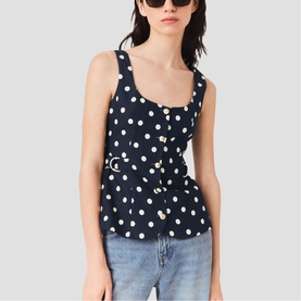 Model wearing Maje navy dots print sleeveless top with gold-tone belted waist, styled with light blue jeans and black sunglasses.