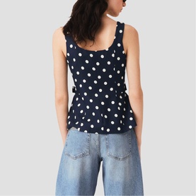 Model wearing Maje navy dots print sleeveless peplum top, back view, styled with light-wash wide-leg jeans