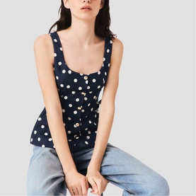 Model wearing Maje navy dots print sleeveless top with button front detail, styled with light blue jeans.
