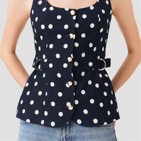 Model wearing Maje navy dots print sleeveless peplum top with gold button detail and D-ring belt, styled with light blue jeans