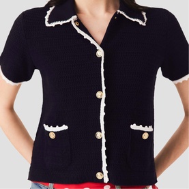 Model wearing Maje navy blue short-sleeve knit cardigan with white frill trim, gold buttons, and front patch pockets