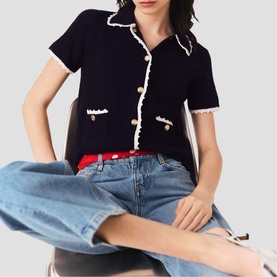 Model wearing Maje navy short-sleeve knit cardigan with white trim, gold buttons, and front pockets, styled with blue jeans and red belt