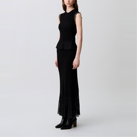 Model wearing Claude Pierlot Rib Knit Top in black, sleeveless with sheer ruffle armhole detail and flared sheer knit hem, styled with a black maxi