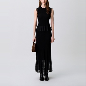 Model wearing Claude Pierlot Rib Knit Top in black, sleeveless with sheer ruffled armholes and flared knit hem, styled with black maxi skirt and boots