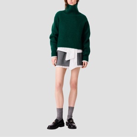 Model wearing Maje bottle green chunky knit turtleneck sweater, styled with white shirt, grey mini skirt and black loafers