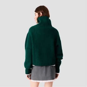 Model wearing Maje bottle green chunky turtleneck sweater, back view, styled with grey mini skirt