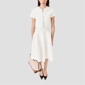 Model wearing Maje metallic white short-sleeve cropped jacket and midi skirt, styled with black pointed heels and a nude bag.