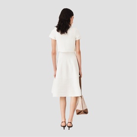 Model wearing Maje metallic white midi dress with short sleeves and belted waist, styled with black heels and a nude shoulder bag.