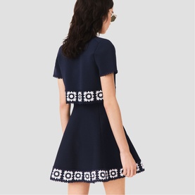 Model wearing Maje navy mini dress with white crochet floral trim at waist and hem, short sleeves, flared skirt, back view