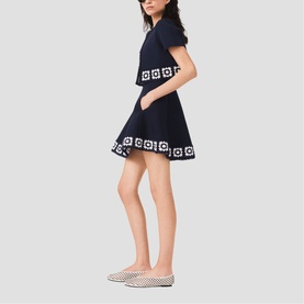 Model wearing Maje navy mini dress with white geometric border trim, styled with white printed flat shoes