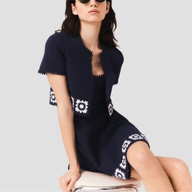 Model wearing Maje navy knit mini dress with white crochet floral patches, styled with matching cropped cardigan and sunglasses