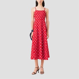 Model wearing Maje Womens French Dress in red dots print, midi length with thin straps and flared skirt, styled with black heels and navy bag.