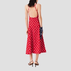 Model wearing Maje French Dress in red dots print, backless halter midi style with flared skirt, styled with black heeled sandals and navy clutch.