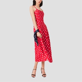 Model wearing Maje French Dress in red polka dot print, midi length with thin straps, styled with black heeled sandals and navy clutch bag.