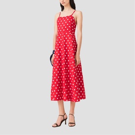 Model wearing Maje Womens French Dress in red dots print, midi length with thin straps, styled with black heeled sandals and dark clutch bag.