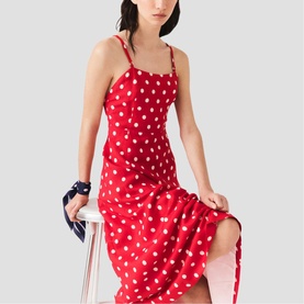 Model wearing Maje Womens French Dress in red dots print, midi length with spaghetti straps, seated pose styled with navy accessories.