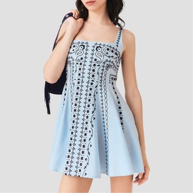 Model wearing Maje Womens French Dress in light blue with black bandana print, flared skirt and square neck, styled with dark bag.