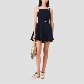 Model wearing Maje Womens French Dress in navy, spaghetti straps, flared skirt, gold hardware detail, styled with cream bag and white trainers.