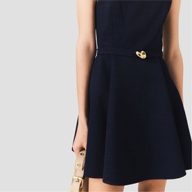 Model wearing Maje Womens French Dress in navy, featuring gold logo hardware at waist, A-line silhouette, styled with a beige bag.