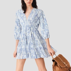 Model wearing Maje sky blue large floral print mini dress with V-neck, 3/4 puff sleeves and tiered skirt, styled with tan leather bag