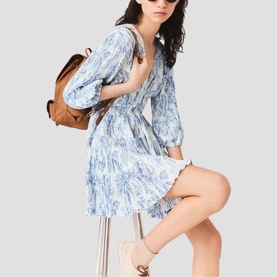 Model wearing Maje sky blue large floral print mini dress with puff sleeves, styled with tan backpack and white trainers