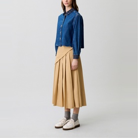 Model wearing Claude Pierlot Pleated Drape Skirt in clear beige, midi-length with side pleats, styled with a denim jacket and white loafers.