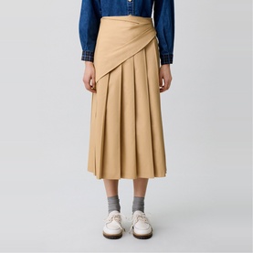 Model wearing Claude Pierlot Pleated Drape Skirt in clear beige cotton midi length with draped wrap detail, styled with denim jacket and white loafers